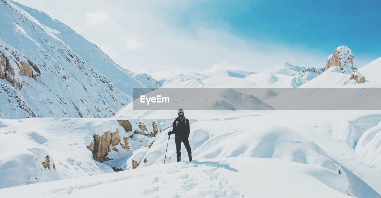 Young man standing on snowy field against sky