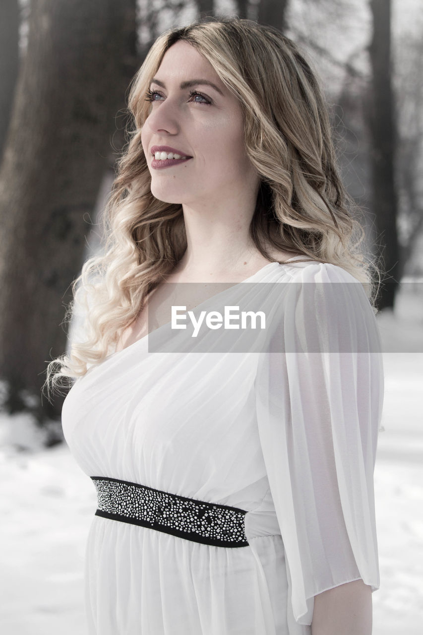 Smiling young woman looking away while standing on snow covered field