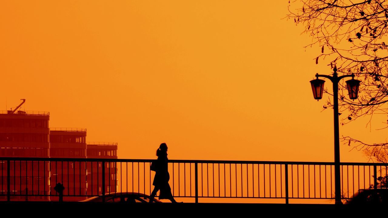 Silhouette woman on sidewalk against orange color