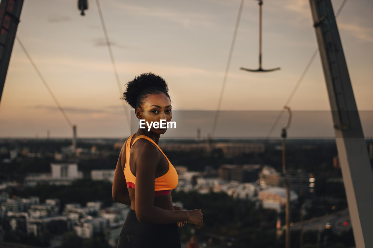 Portrait of female athlete against sky during sunset