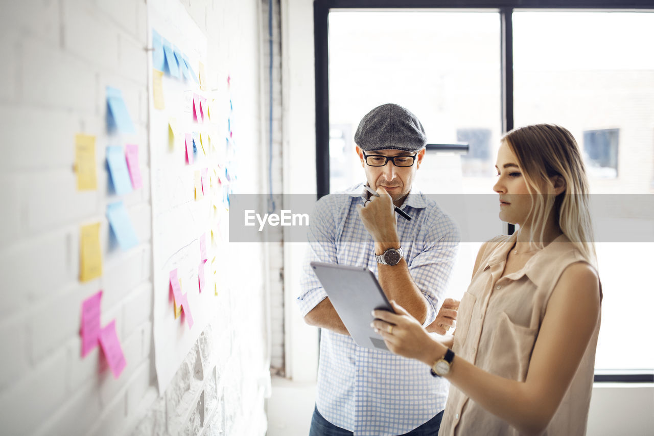 Businesswoman showing tablet computer to male colleague at creative office