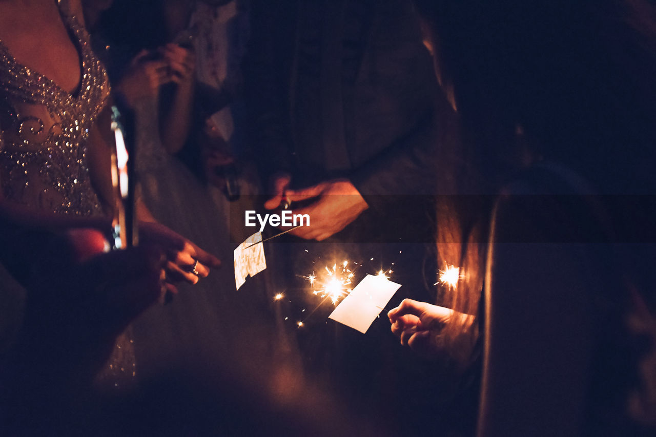 Midsection of people holding illuminated sparklers at night