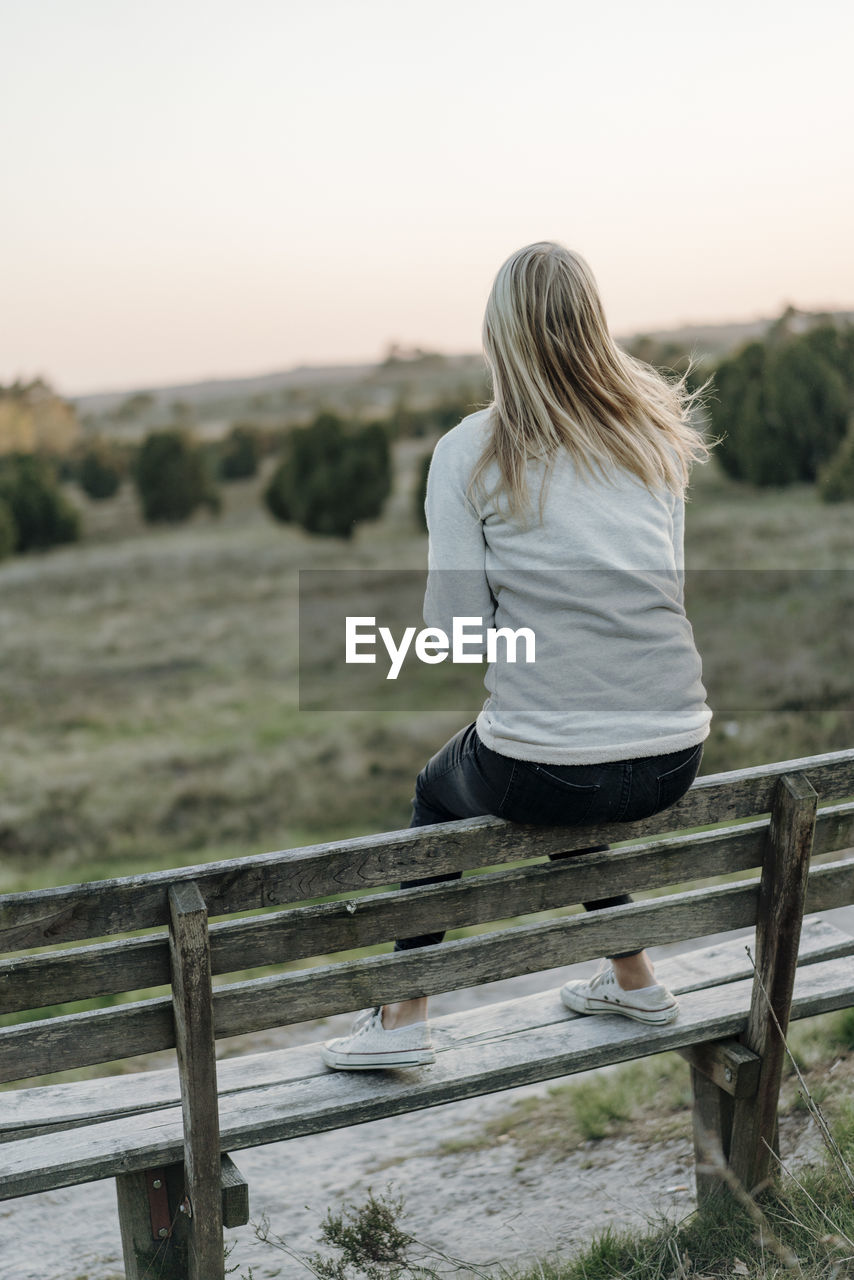 Full length of woman looking at view while sitting on bench during sunset