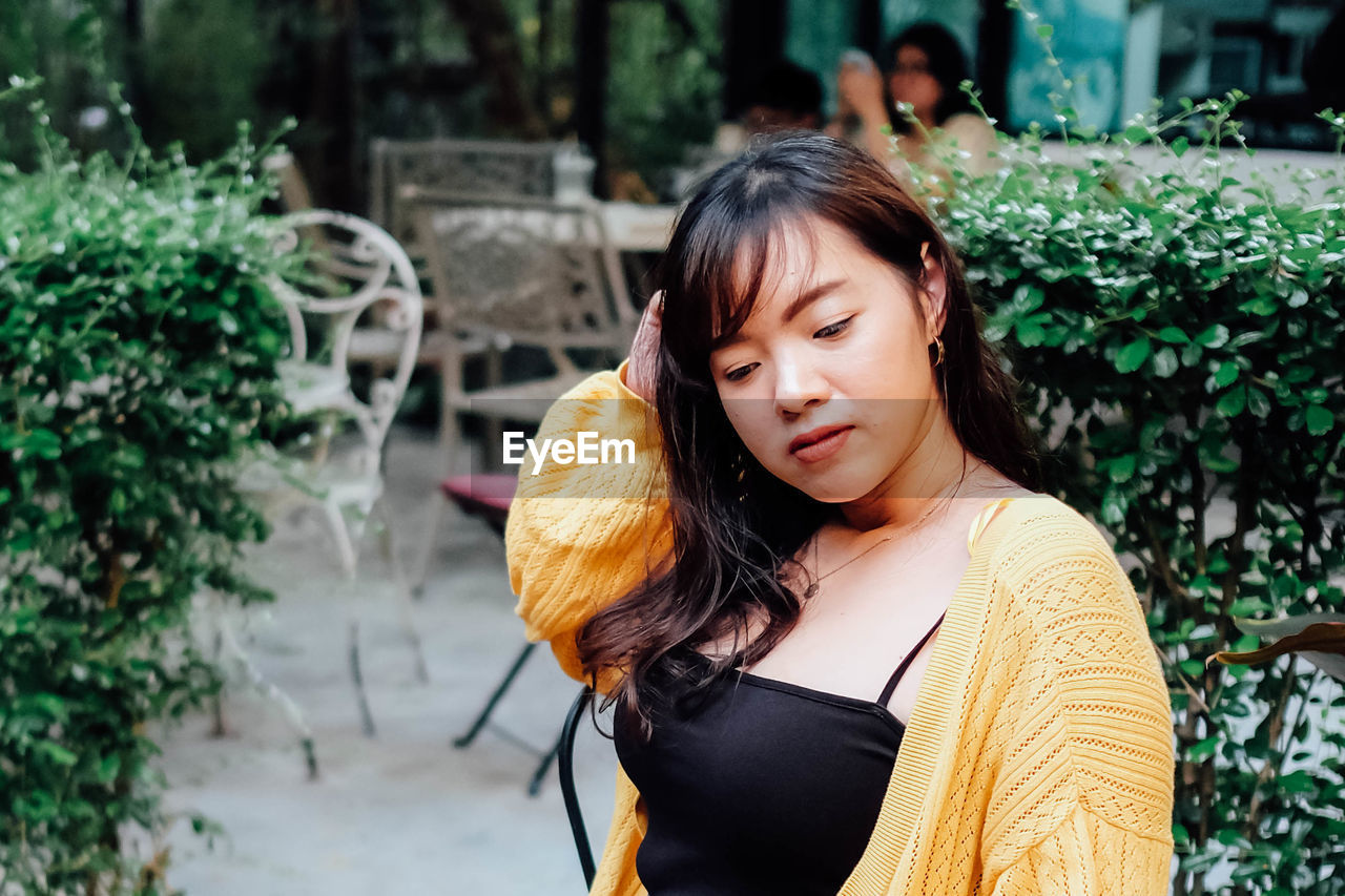 Close up of young pretty asian woman in blue yellow sweater with garden background.