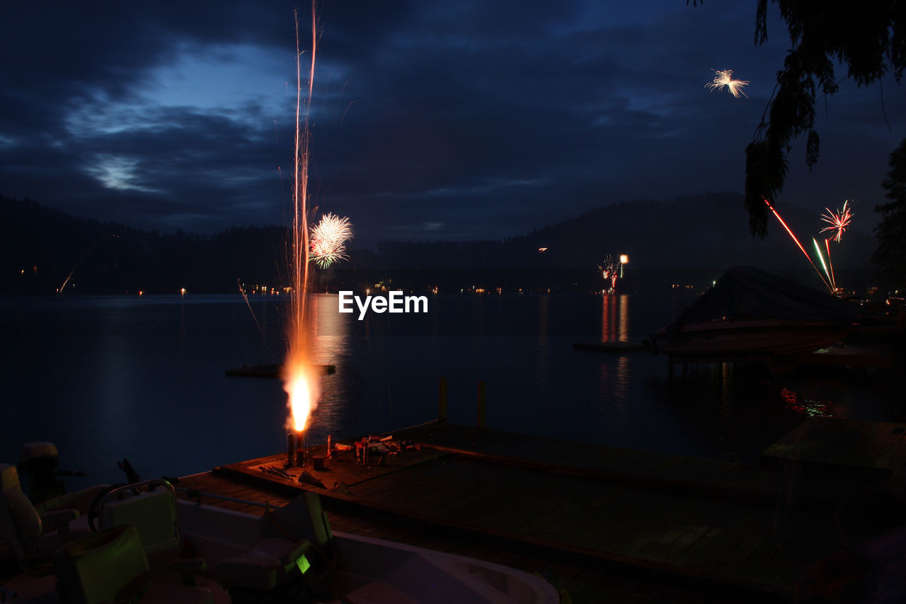 Fireworks exploding on pier by lake at night