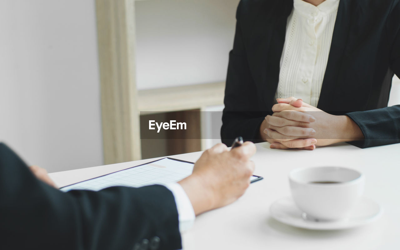 Midsection of colleagues by coffee cup on table