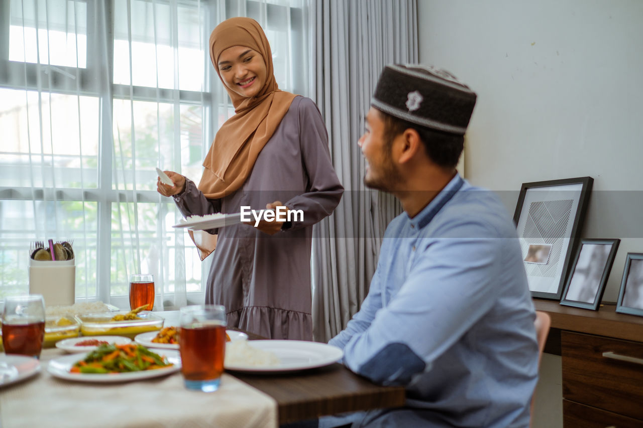 Smiling woman holding serving food to husband at home