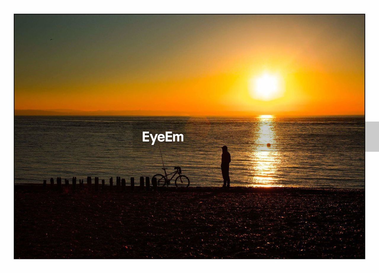 Silhouette man standing on shore at beach during sunset