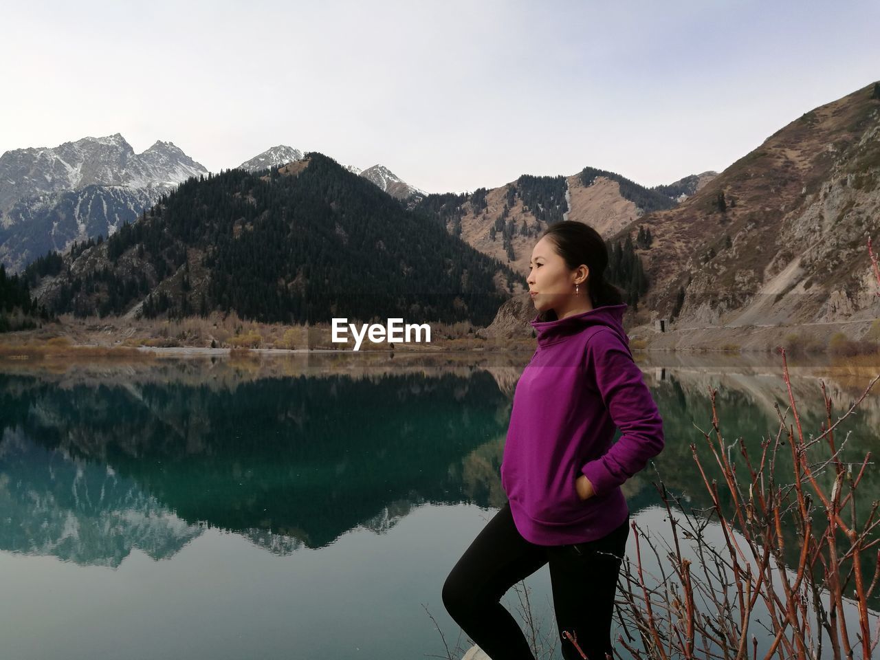 Side view of young woman standing by lake against mountains