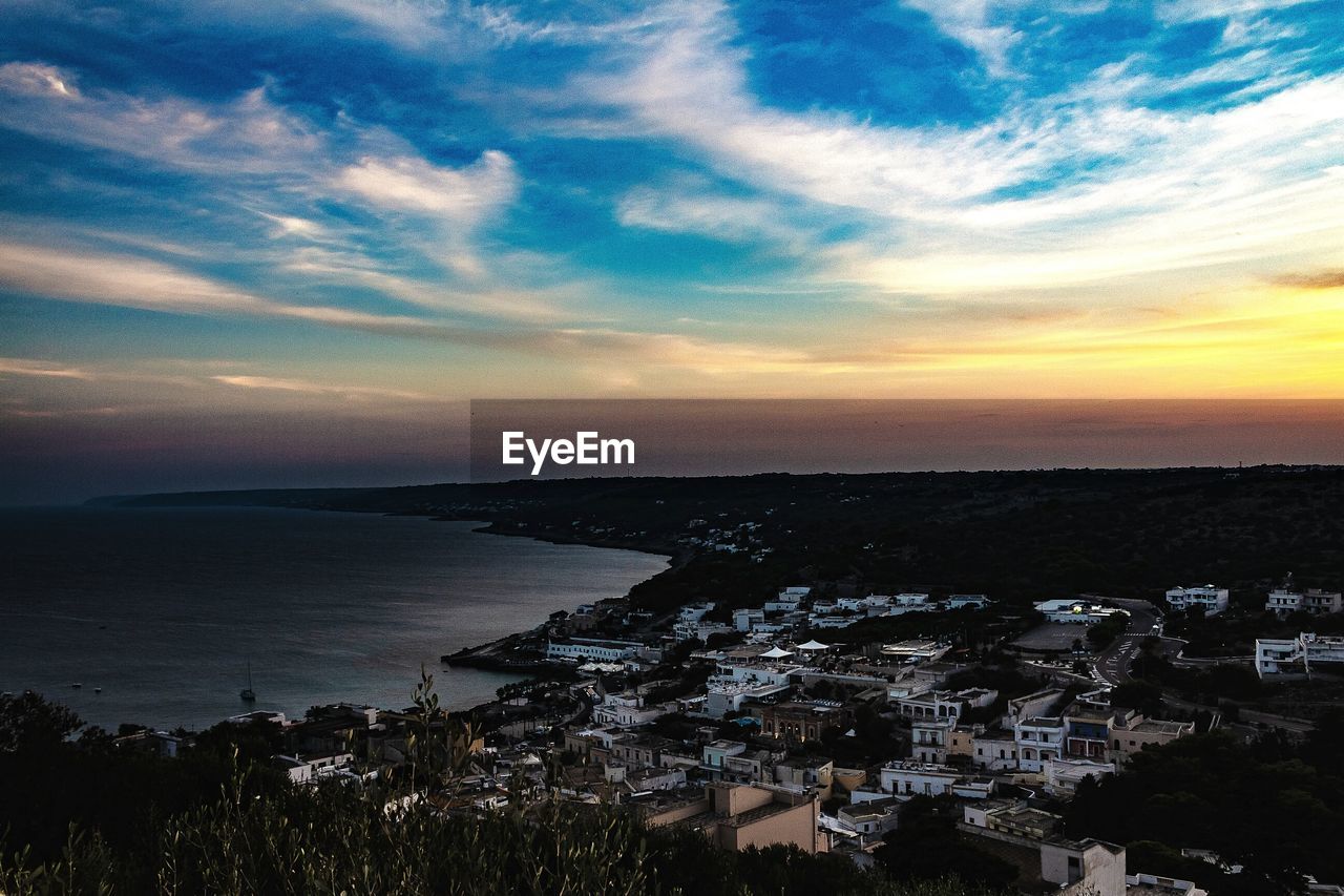 HIGH ANGLE VIEW OF TOWNSCAPE BY SEA DURING SUNSET