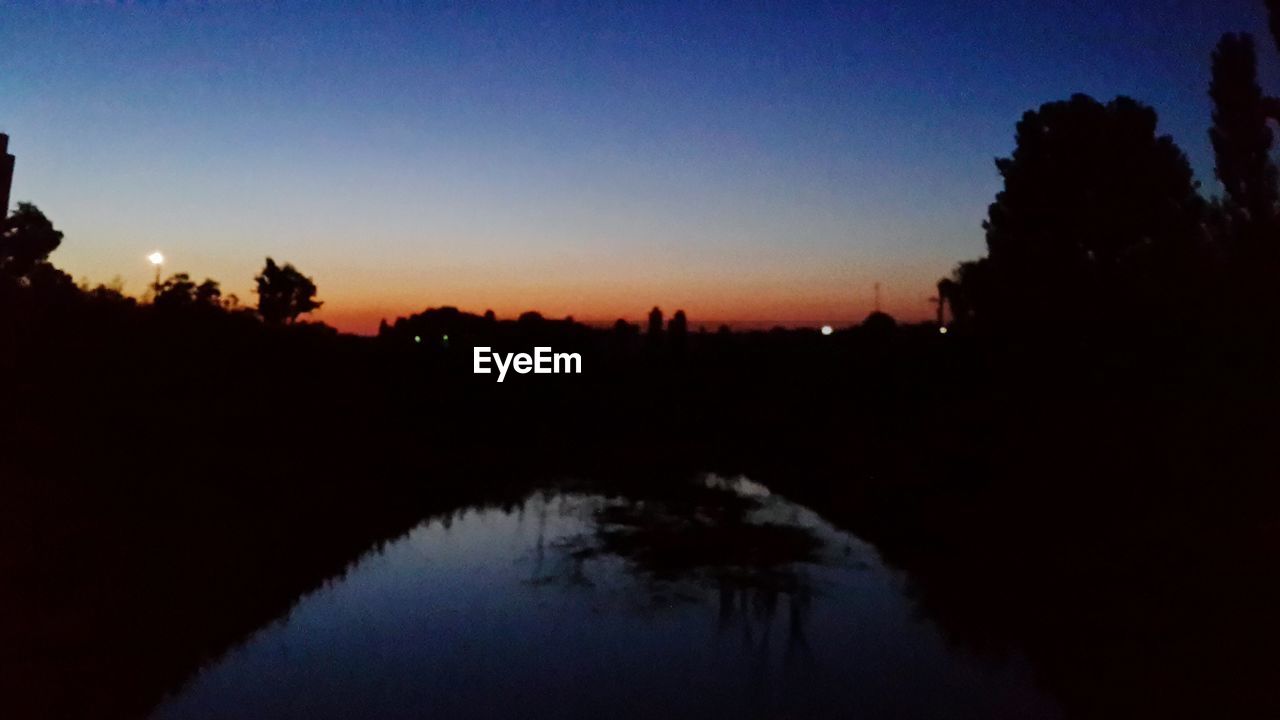 SILHOUETTE TREES BY LAKE AGAINST ORANGE SKY