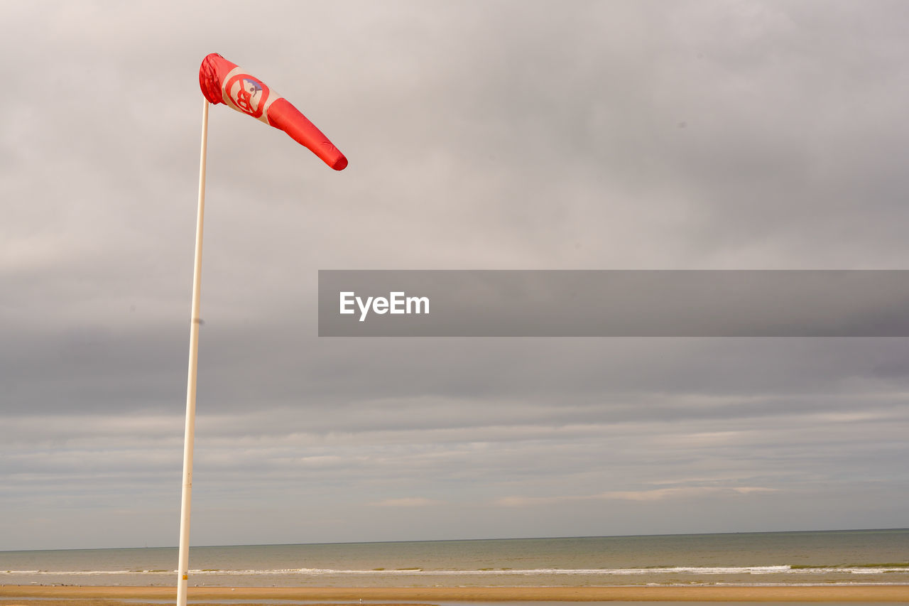 sky, cloud, water, sea, nature, wind, land, beach, beauty in nature, horizon, horizon over water, scenics - nature, flag, environment, day, red, tranquility, sports, windsports, tranquil scene, outdoors, no people, toy, coast, motion, sand, ocean