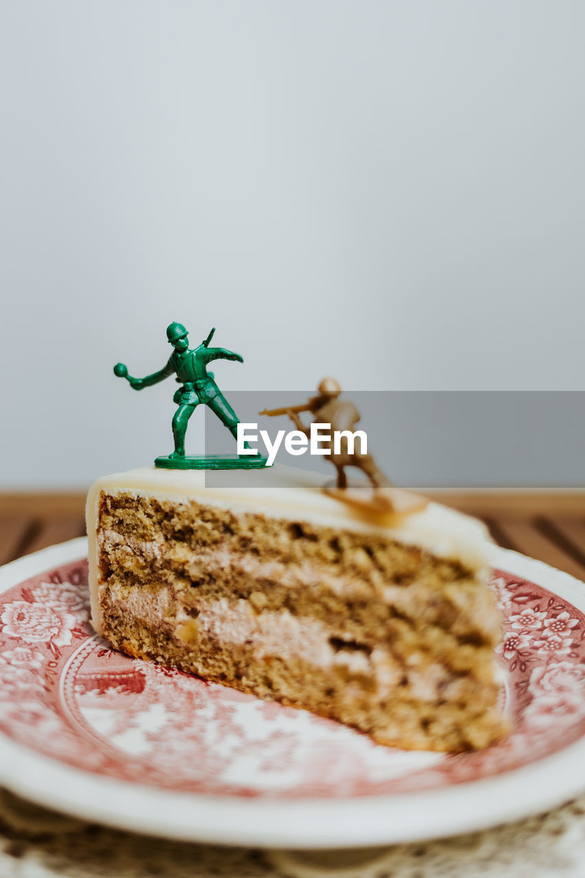 Two toy soldiers fighting on the top of a piece of cake on a plate - white background - close up