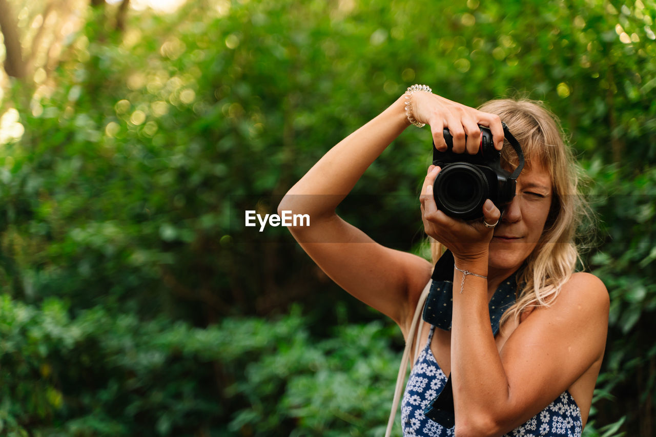 Blonde woman taking a picture standing in a park