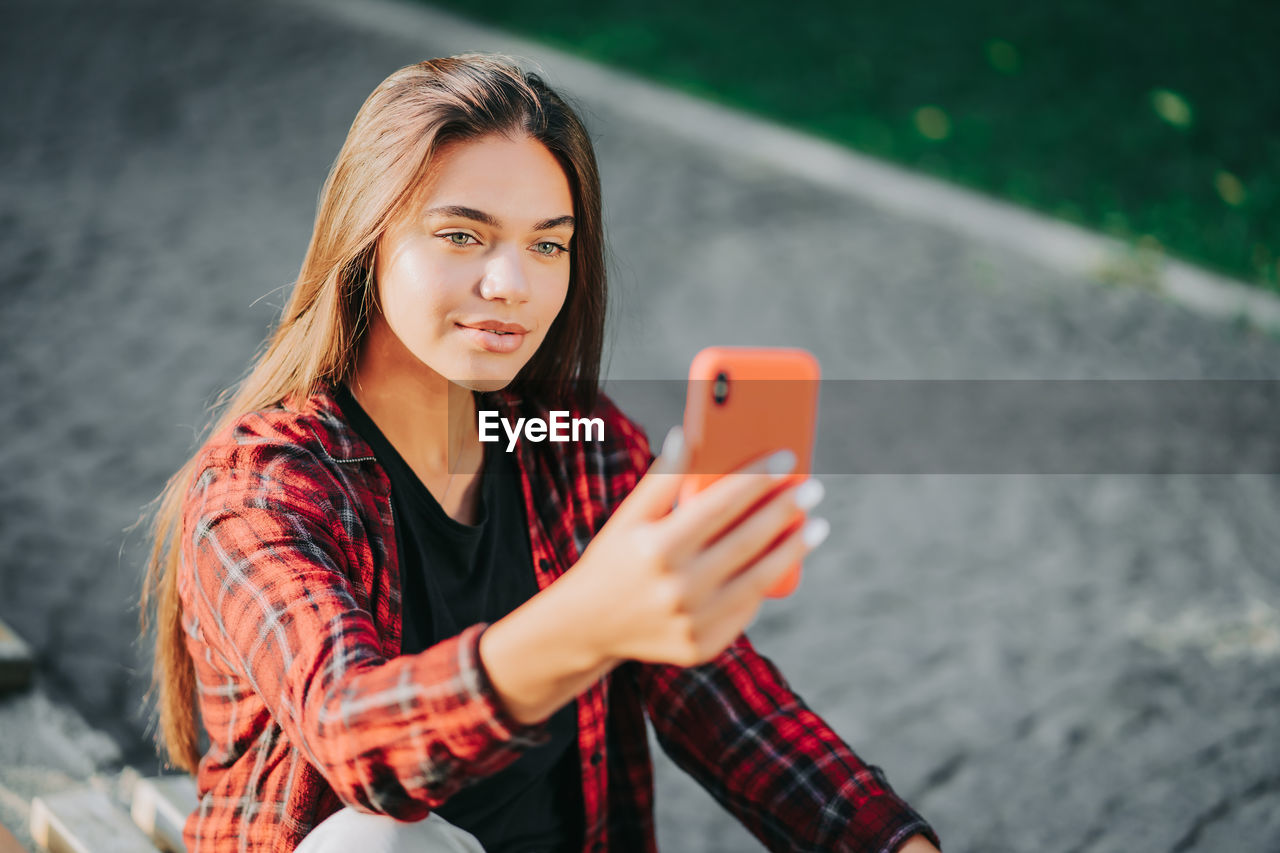 Smiling woman using mobile phone while sitting at bench in park