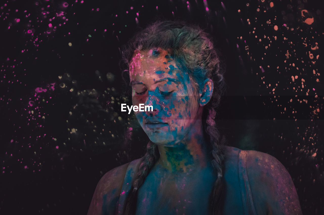 Close-up of woman with powder paint on face against black background