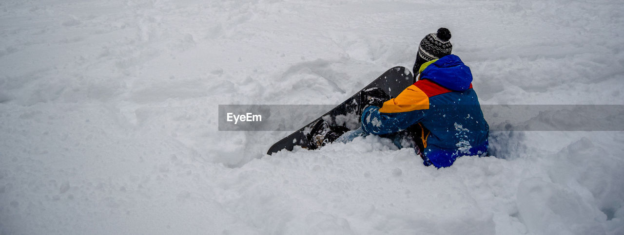 Person with snowboard sitting on snow covered field