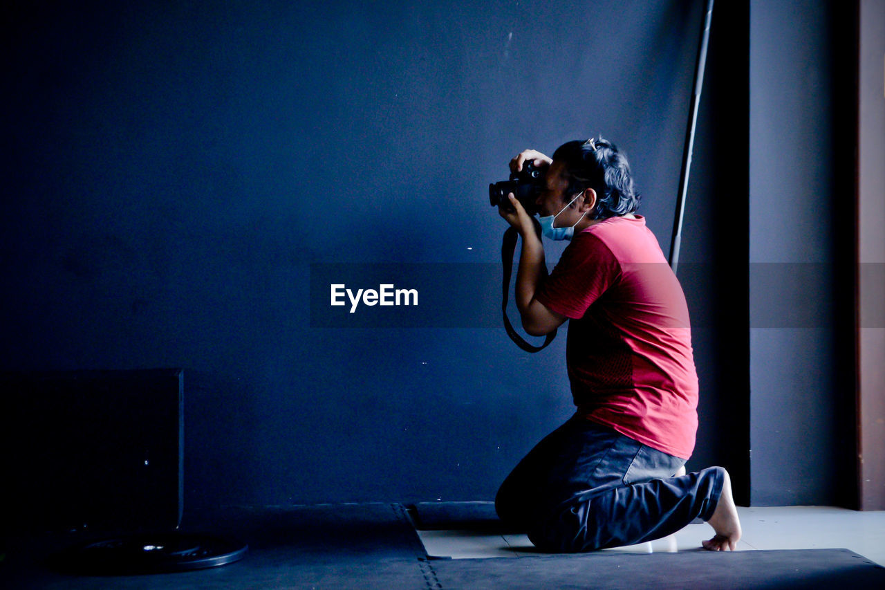 Man photographing while sitting against blue wall