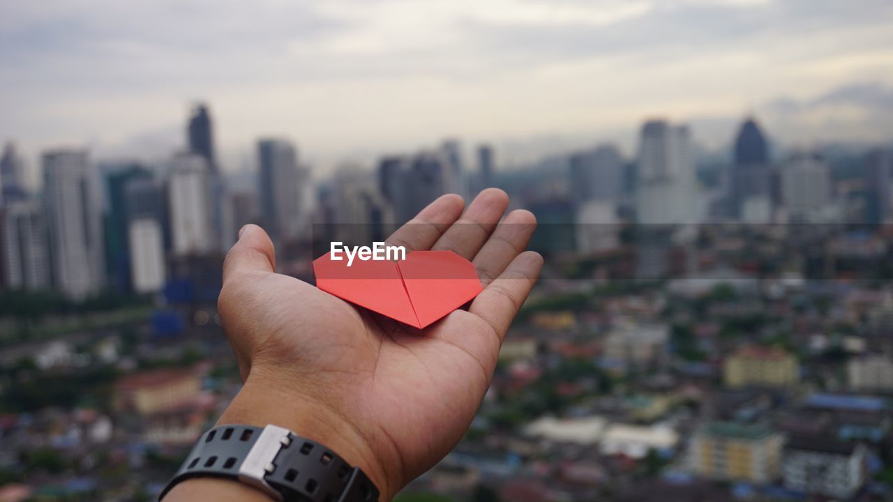 Close-up of hand holding heart shape against cityscape