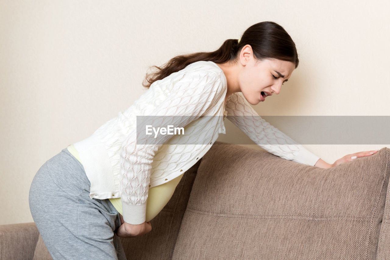 Side view of young woman against wall at home