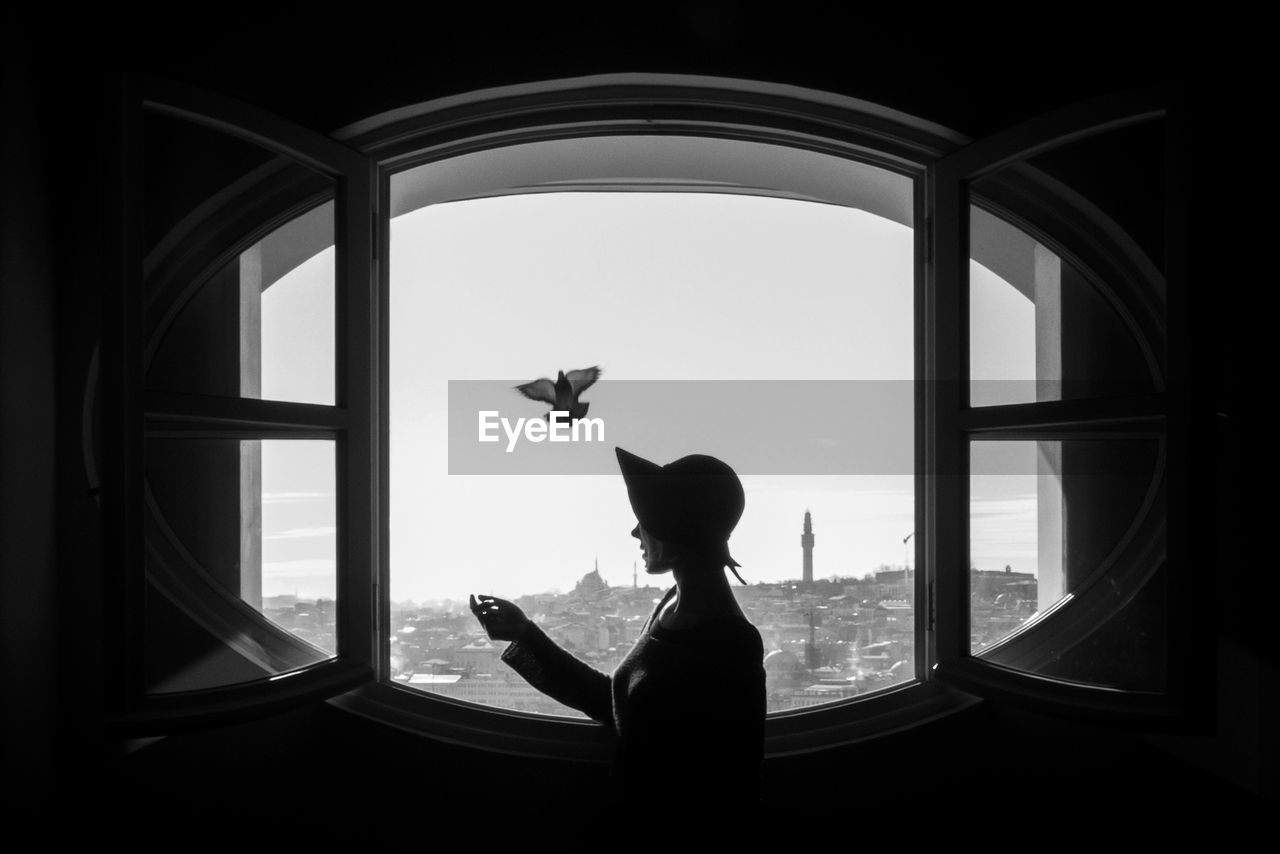 Side view of woman looking at cityscape through window