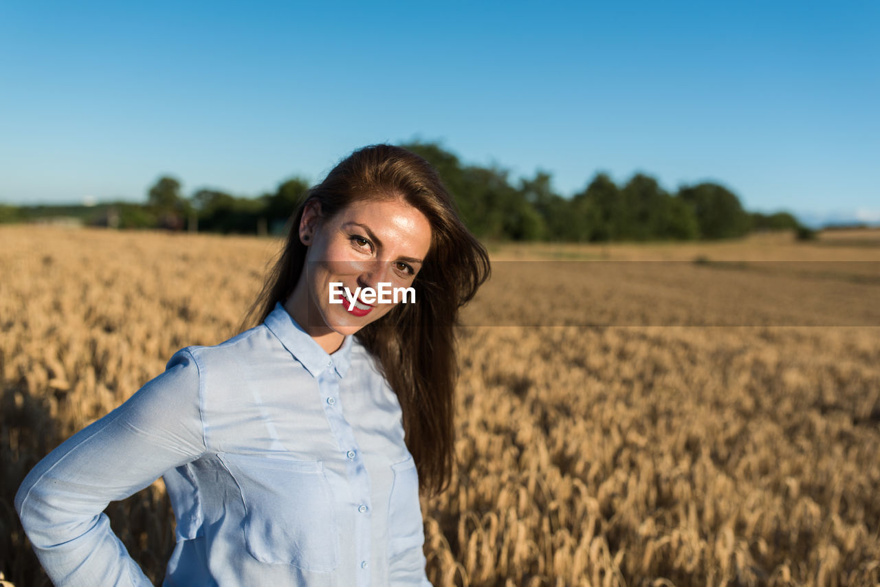 Portrait of beautiful woman standing against wheat field