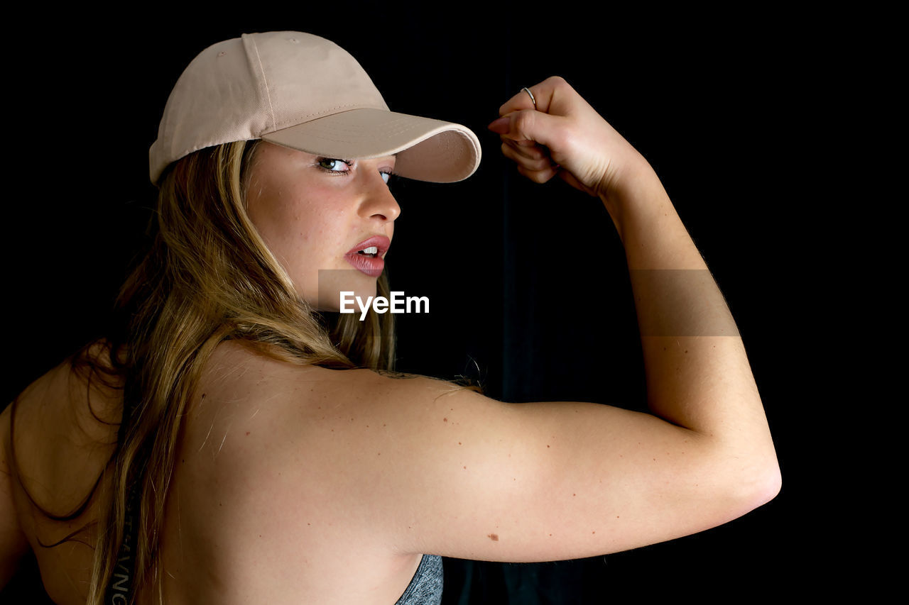 Beautiful young woman flexing muscles against black background