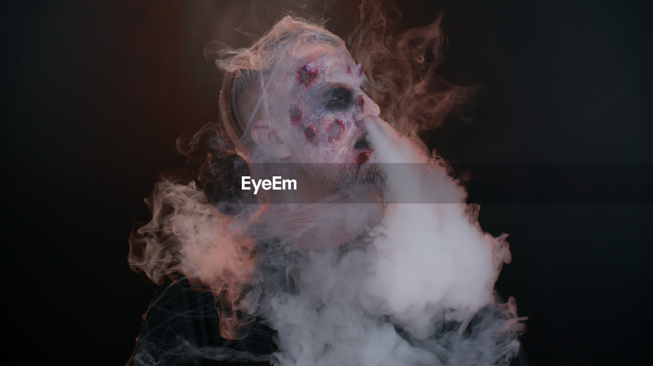 Portrait of man smoking against black background