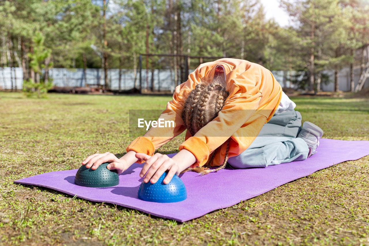 A girl teenager goes in for sports in nature, does stretching on a sports mat on a summer sunny day