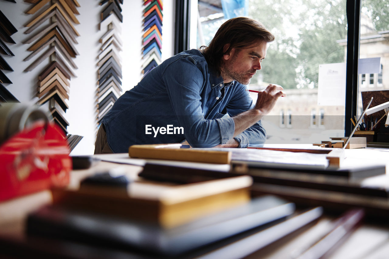 Mature male store owner using laptop leaning on table while working in store