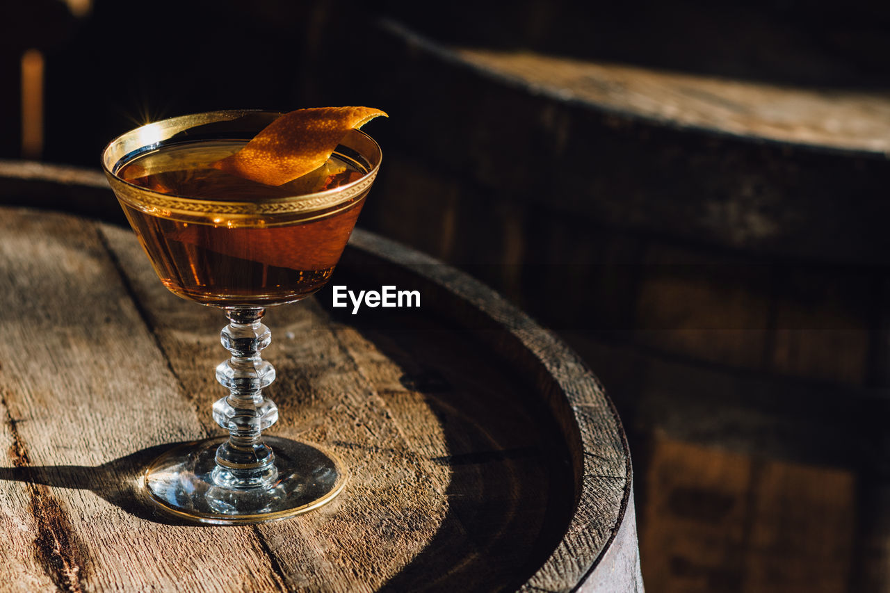 Manhattan bourbon whiskey cocktail in vintage crystal hotel glass orange garnish atop wood barrel