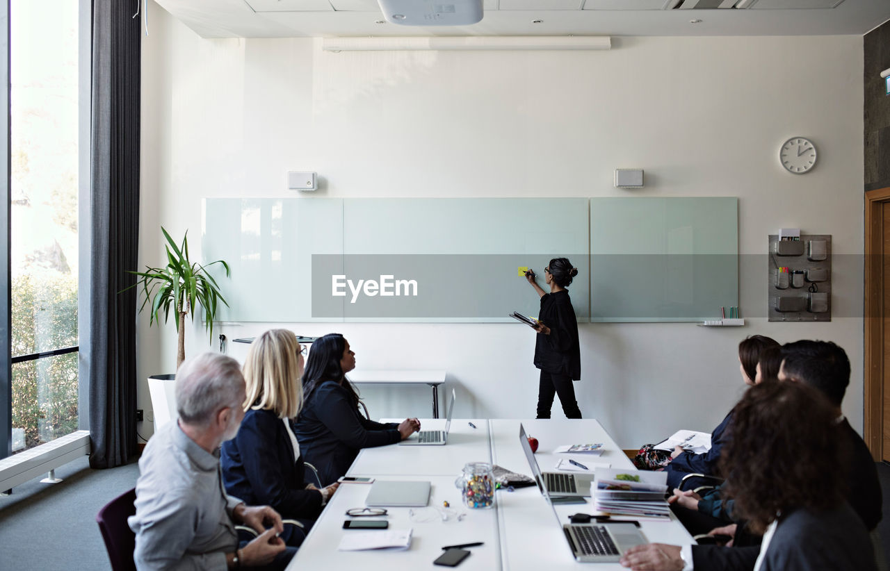 Colleagues concentrating on businesswoman giving presentation during meeting in office