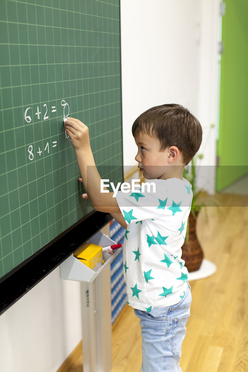 Cute boy writing on blackboard in classroom