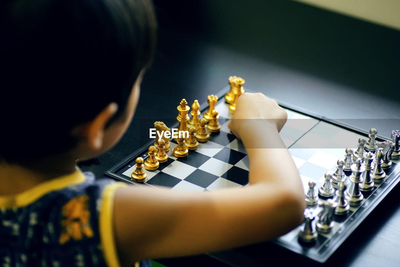 Rear view of boy playing chess at table