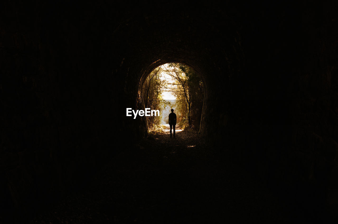 Silhouette man standing in tunnel at forest