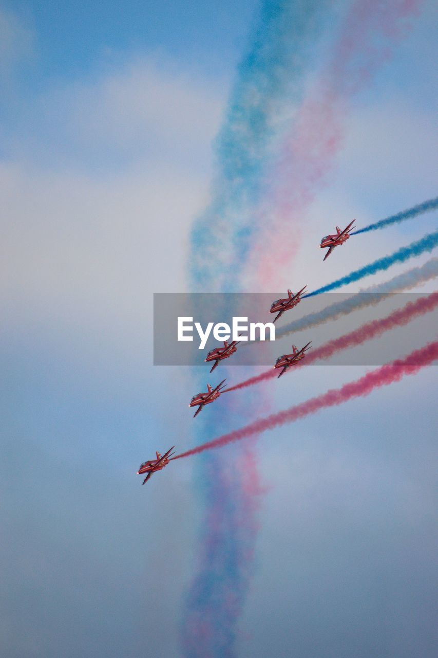 Red arrows in formation with red white and blue vapor trail in sky perform at airshow