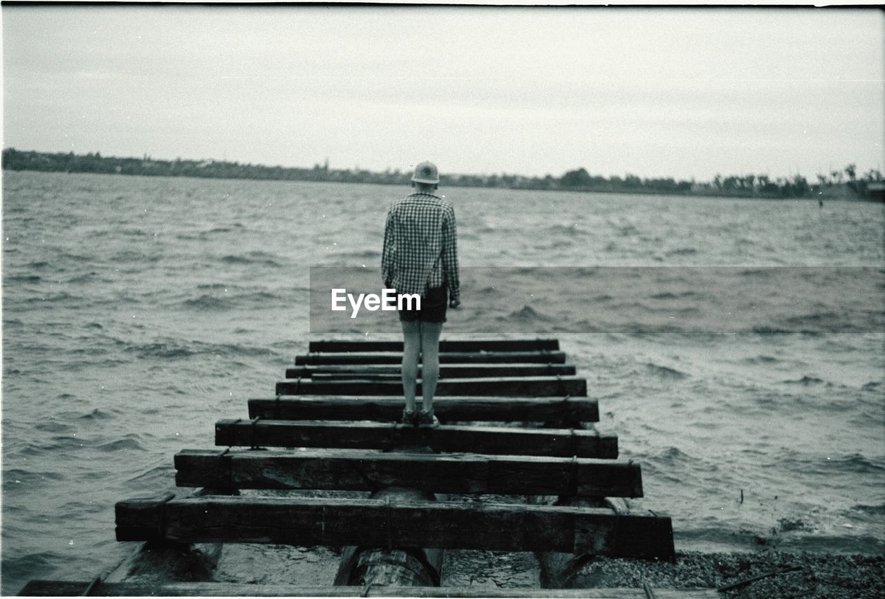 Rear view of a man standing on jetty overlooking lake