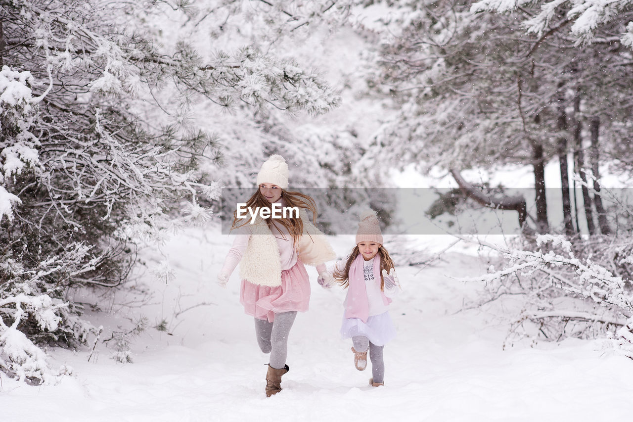 Full length of sisters holding hands walking on snow covered land