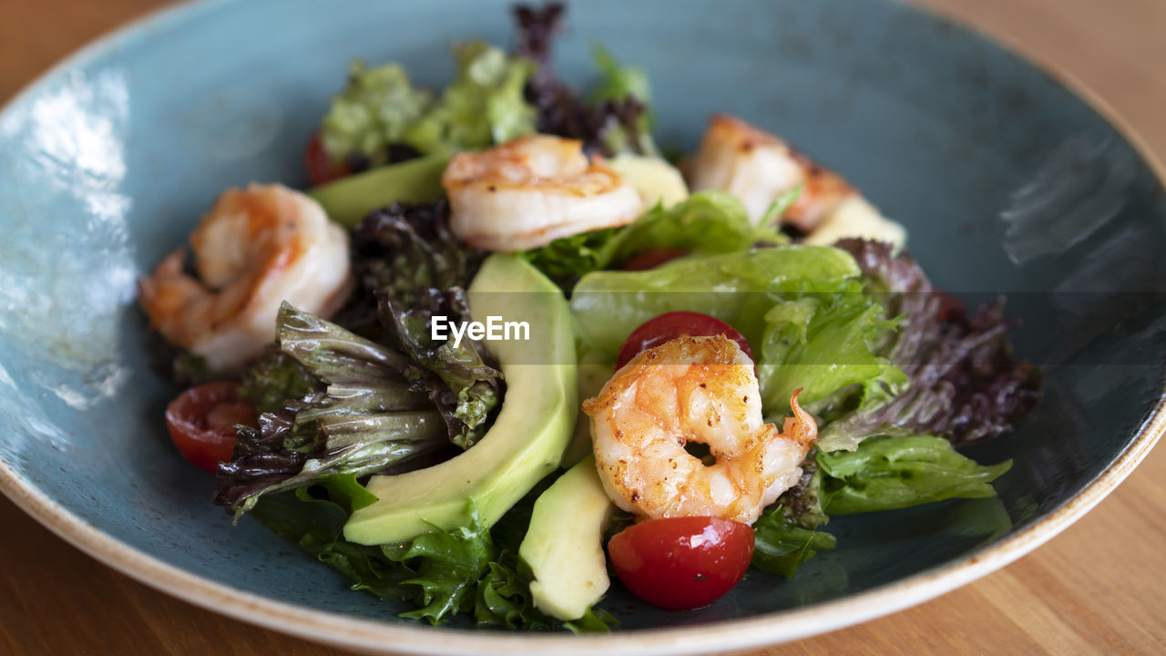 Salad with fresh avocado, lettuce, grilled shrimps, cucumeber on blue dish. healthy eating.