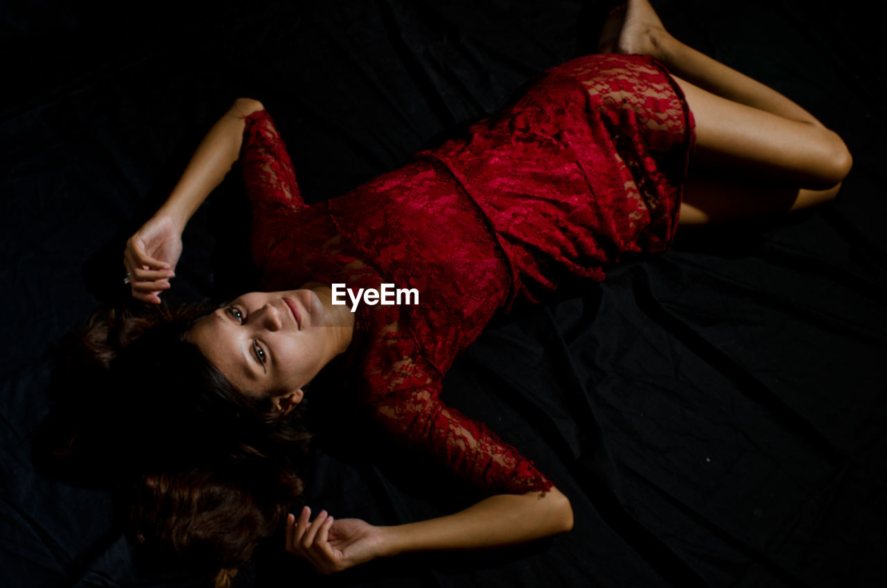 High angle view of beautiful woman wearing red dress while lying on bed at home