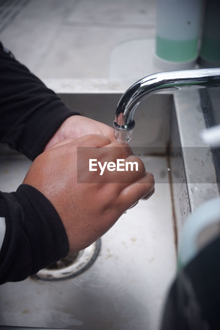 CLOSE-UP OF HAND HOLDING WATER AT FAUCET