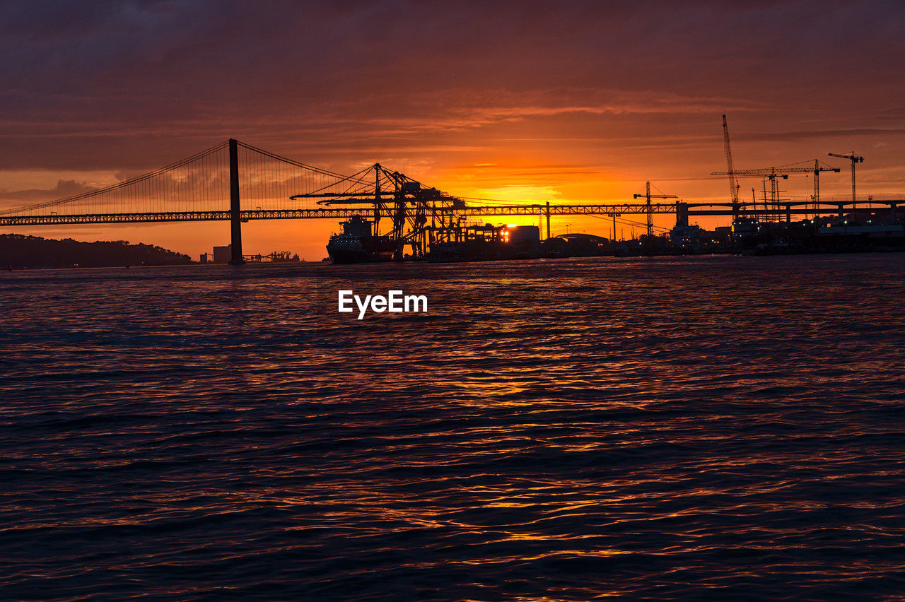 water, transportation, sky, sea, architecture, sunset, bridge, industry, dusk, built structure, evening, nature, horizon, engineering, ocean, machinery, crane - construction machinery, suspension bridge, business finance and industry, business, reflection, freight transportation, shipping, cloud, beauty in nature, nautical vessel, dramatic sky, travel destinations, mode of transportation, city, vehicle, outdoors, silhouette, cargo container, coast, container, pier, harbor, travel, wave, ship, scenics - nature, construction industry, copy space, environment, moody sky