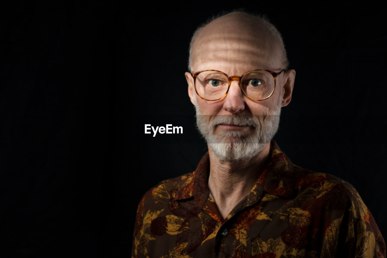 Portrait of senior man wearing eyeglasses against black background