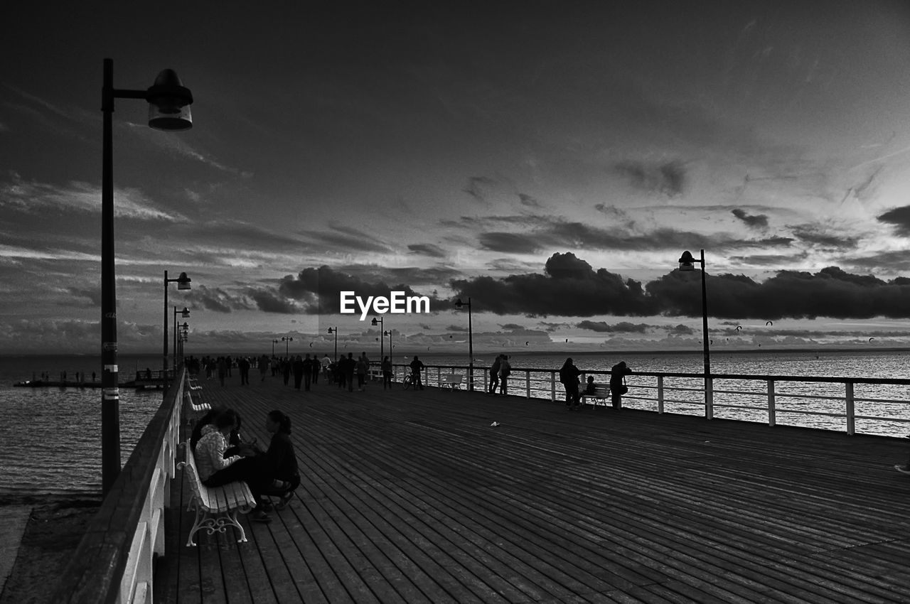 People on pier over sea against sky