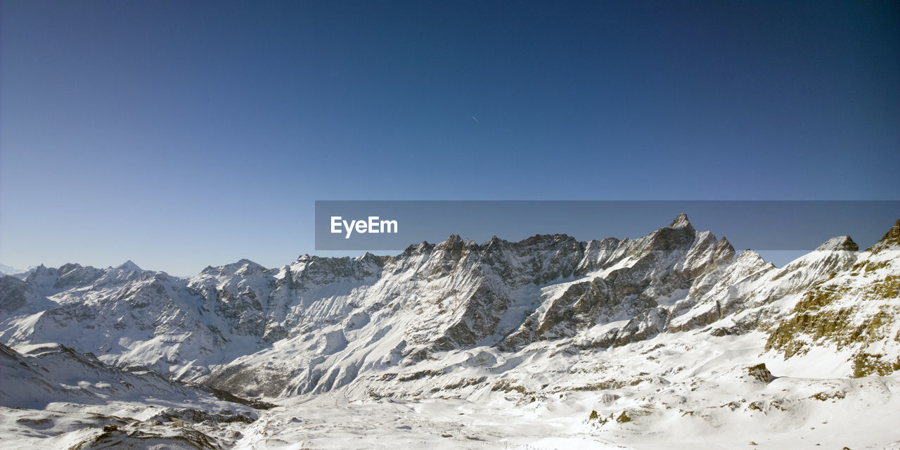 Low angle view of snowcapped mountains against clear blue sky