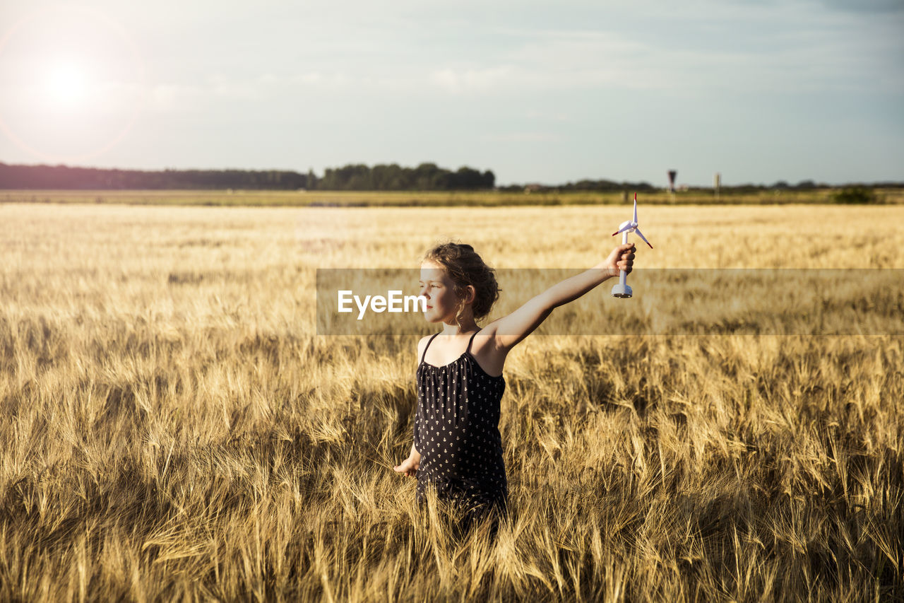 Girl standing in grain field holding miniature wind turbine