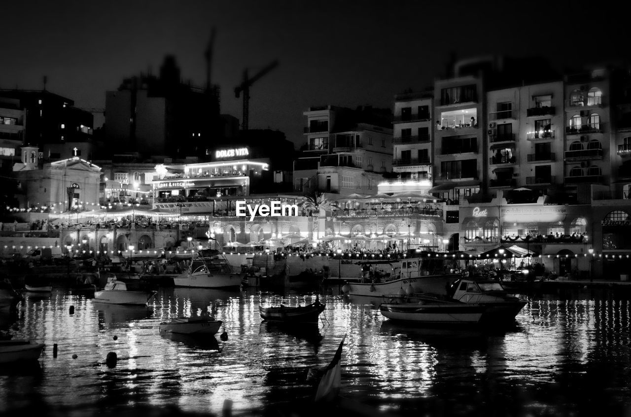 Boats moored in river against illuminated city at night