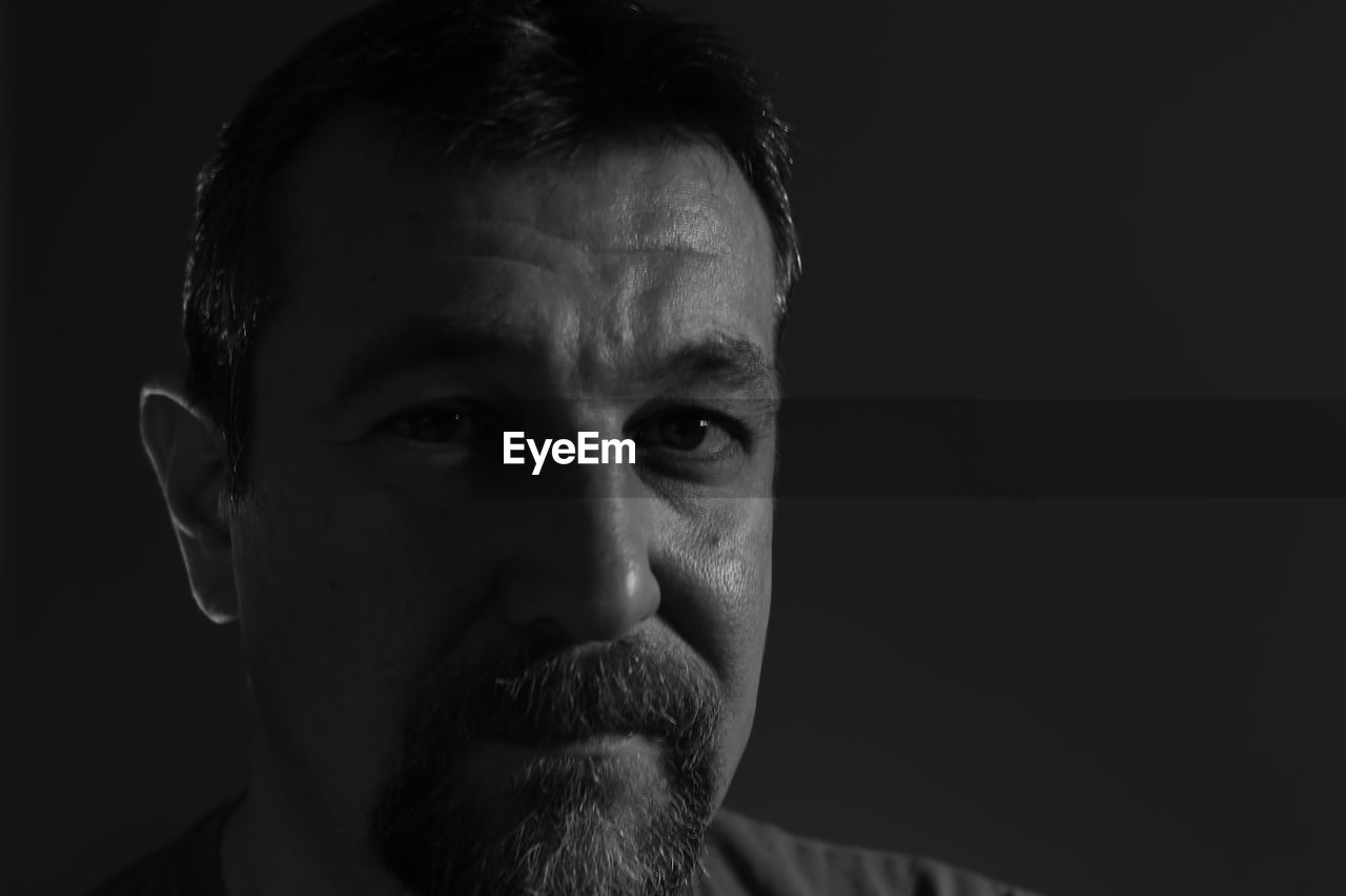 Close-up portrait of mature man against black background