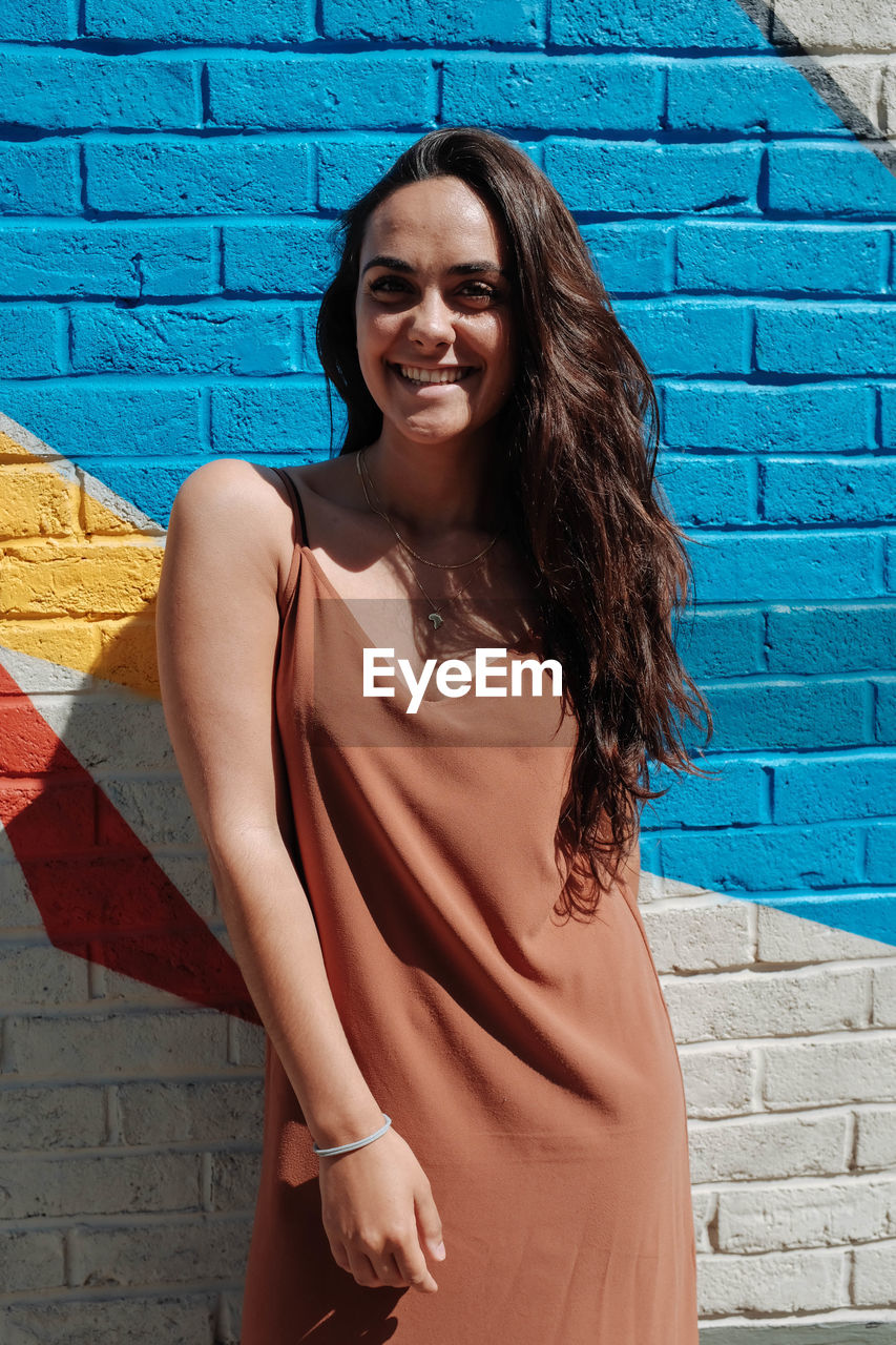 Portrait of happy young woman standing against wall