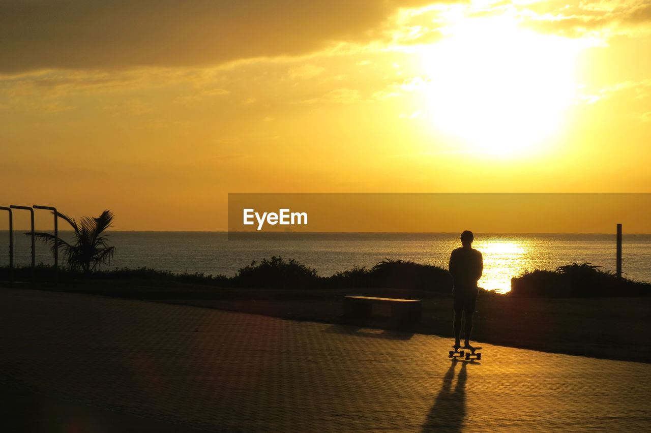 SILHOUETTE MAN LOOKING AT SEA DURING SUNSET